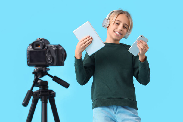 青い背景にビデオを記録するガジェットとヘッドフォンのティーンエイジャーブロガー - 写真・画像