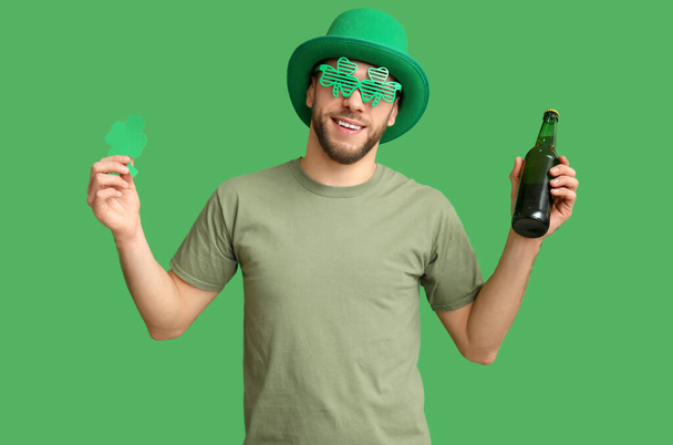 Молодой человек в шляпе лепрекона с бутылкой пива и клевером на зеленом фоне. Празднование Дня Святого Патрика - Фото, изображение