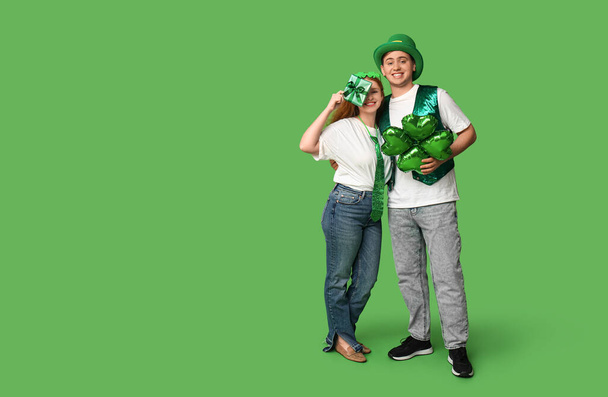Young couple with gift and balloon in shape of clover on green background. St. Patrick's Day celebration - Photo, Image