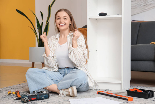 Schöne junge glückliche Frau montiert weiße Regaleinheit zu Hause - Foto, Bild