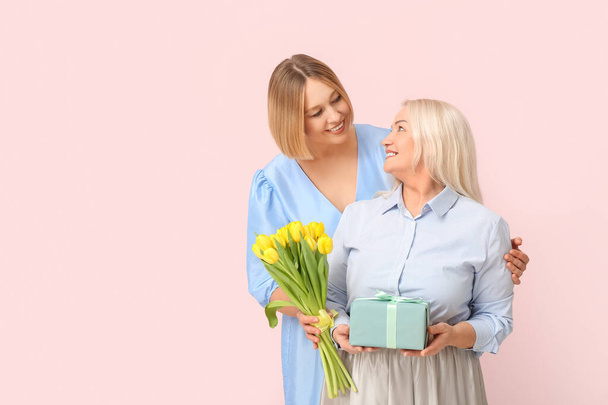Доросла жінка зі своєю матір'ю, букет тюльпанів і подарункова коробка на рожевому тлі. Міжнародний жіночий день - Фото, зображення