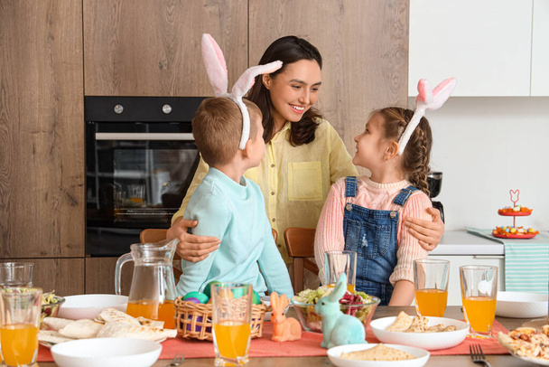 Mère heureuse embrassant ses petits enfants au dîner de Pâques dans la cuisine - Photo, image