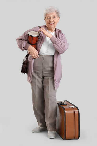 Turista femenina senior con tambor y bolsas sobre fondo claro - Foto, Imagen