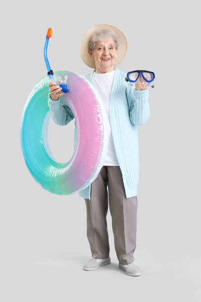 Seniorka turista s plaveckým kroužkem a šnorchlování maska na světlém pozadí - Fotografie, Obrázek