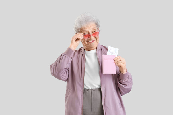 Senior γυναίκα τουρίστρια σε γυαλιά ηλίου με διαβατήριο στο φως φόντο - Φωτογραφία, εικόνα