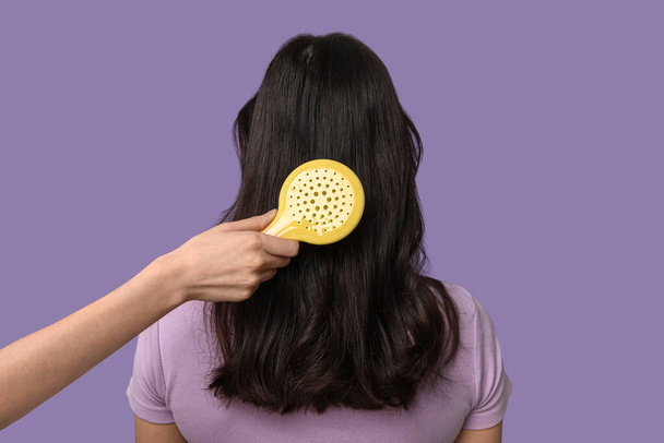 Giovane donna e mano con spazzola per capelli su sfondo lilla, vista posteriore - Foto, immagini