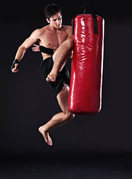 Bojová umění, muž a trénink s kolenem v boxovací tašce pro rozvoj dovedností v temném ateliéru s mocí. Muž osoba, postava a černé pozadí v tělocvičně pro fitness, muay thajský skok a sílu. - Fotografie, Obrázek