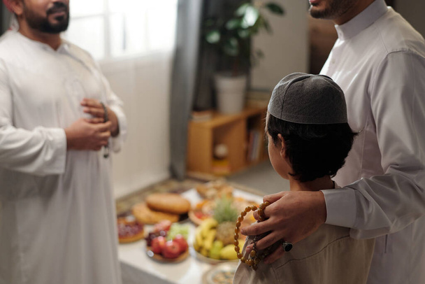 Selectieve focusshot van trotse moslimvader en zijn zoon in gesprek met mannelijk familielid bij familiebijeenkomst op Eid Al-Fitr, kopieer ruimte - Foto, afbeelding