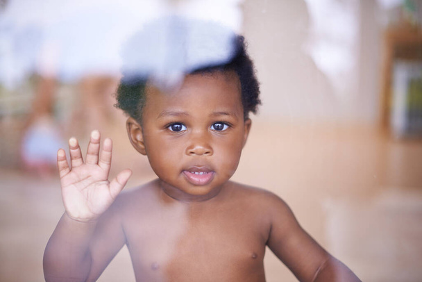 Bébé, portrait et sourire derrière la fenêtre, développement naturel et infantile pour la croissance des tout-petits dans la maison familiale. Enfants, éducation sensorielle et toucher la main sur le verre, curieux jeu avec un jeune garçon africain. - Photo, image