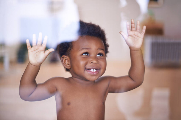 Ребенок, счастливый и улыбающийся за окном, естественное и детское развитие для роста малыша в семейном доме. Дети, сенсорное образование и прикосновения рукой к стеклу, любопытная игра с маленьким африканским мальчиком. - Фото, изображение