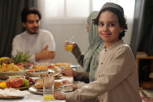 Selektywny portret skupienia szczęśliwego muzułmanina siedzącego przy świątecznym stole, patrzącego w kamerę, podczas gdy Uraza Bayram świętuje kolację z rodziną - Zdjęcie, obraz