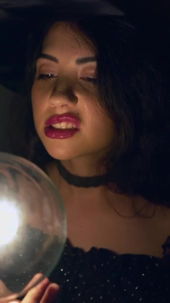 Kaksi kolumbialaista naista halloween-asussa noitahattu päässään liikuttamassa käsiään läpinäkyvän lampun ympärillä pimeässä huoneessa Valenciassa, Espanjassa. - lähikuva Shot - Pystysuora 1080 - Materiaali, video
