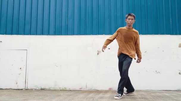 Hispanic man strek armen en dans straat dansen voor de muur. Motion shot van danser of choreograaf in casual outfit oefenen b-boy dansen in hip hop stijl. Outdoor sport 2024. hiphop. - Video