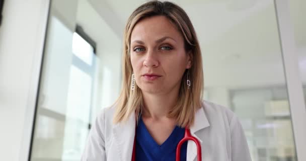Attentive woman doctor with serious face leans toward camera slow motion. Blonde medic in gloves poses for camera with professional demeanor - Footage, Video