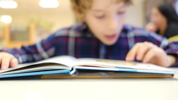 Розмитий маленький хлопчик читає книгу за столом - Кадри, відео