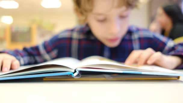 Розмитий маленький хлопчик читає книгу за столом - Кадри, відео