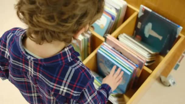 Маленький хлопчик вибирає книжки в бібліотеці - Кадри, відео