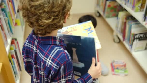 pienet pojat valitsevat kirjoja kirjastossa - Materiaali, video