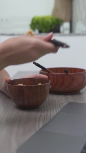 Henkilö syö käyttäen puisia astioita ja kulhoja kannettavan tietokoneen vieressä. Lähikuva - Pystysuora - Materiaali, video