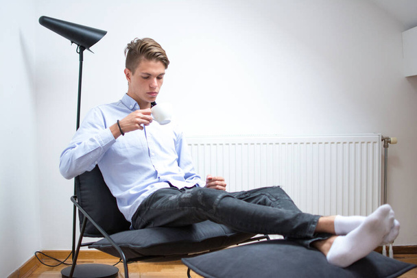 Junger Mann mit einer Kaffeetasse beim Entspannen auf seinem Zimmer - Foto, Bild