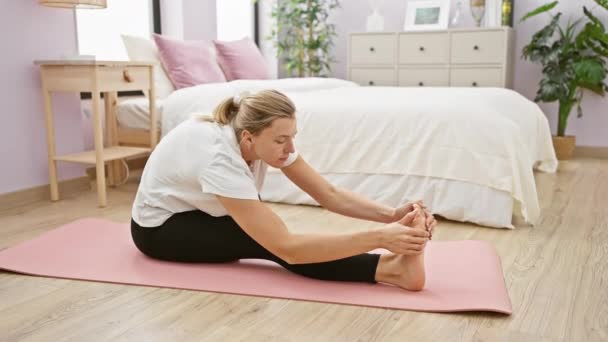 Женщина растягивается на коврике для йоги в спальне, демонстрируя здоровье и фитнес-рутину. - Кадры, видео
