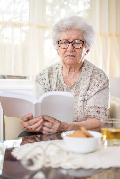 Oudere vrouw leest boek thuis. - Foto, afbeelding