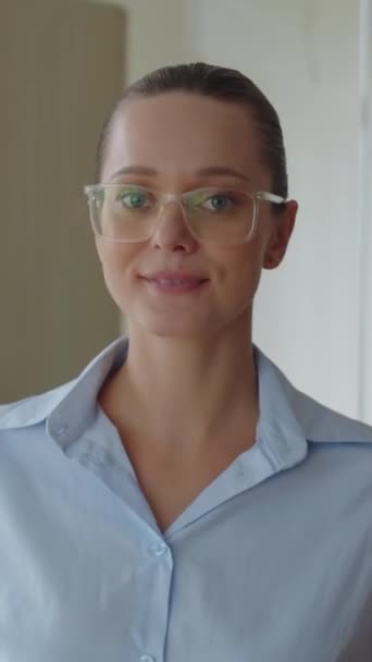 Вертикальный портрет кавказки в очках, смотрящей в камеру в офисе - Кадры, видео