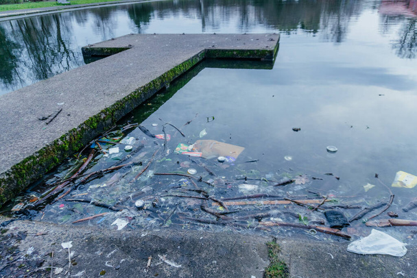 Contaminación de basura en la vía navegable urbana, una variedad de artículos de basura, incluyendo bolsas de plástico, latas y otros desechos flotando en una vía navegable urbana, los desafíos ambientales en los paisajes de nuestra ciudad - Foto, imagen