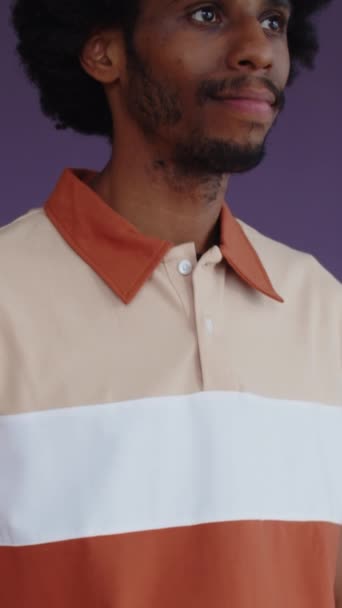 Retrato vertical del joven negro con camiseta a rayas posando para cámara aislada sobre fondo púrpura - Imágenes, Vídeo