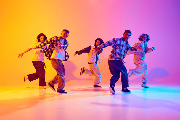 Jovens dançarinos talentosos executando dança streetstyle em movimento em luz de néon contra gradiente colorido estúdio fundo. Conceito de hobby, esporte, moda, ação, cultura juvenil, música e dança. - Foto, Imagem
