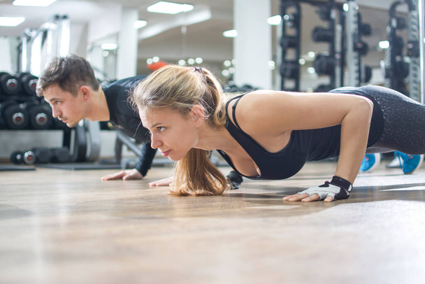 Sporty young woman and man doing push ups together in gym. - Photo, Image