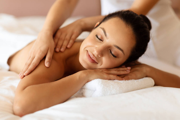 Крупный план женщины-клиента СПА-центра, получающей расслабляющий лечебный массаж, массирует руки мягко, массируя плечи и спину в помещении. Расслабление, уход за телом и благополучие - Фото, изображение