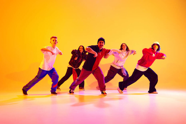 Energetic dance team performing contemporary dance moves in neon light against gradient colorful studio background. Concept of hobby, sport, fashion and style, action, youth culture, music and dance. - Photo, Image