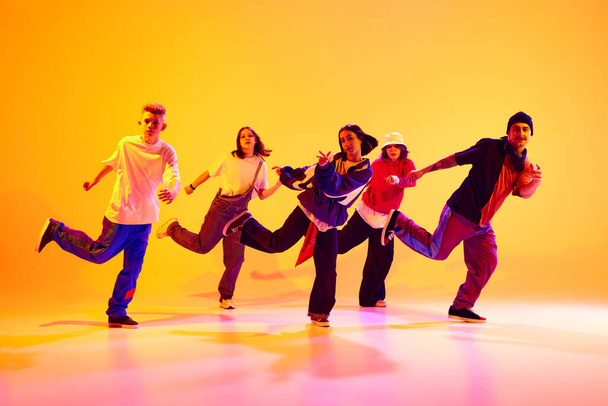 Nowoczesna ekipa taneczna w ruchu synchronicznym wykonująca hip-hop w neonowym świetle na gradientowym kolorowym tle studia. Pojęcie hobby, sportu, mody i stylu, działania, kultury młodzieżowej, muzyki i tańca. - Zdjęcie, obraz