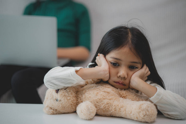 Ein junges Mädchen sitzt auf einer Couch, auf ihrem Schoß ein Teddybär. Sie ist traurig oder verärgert - Foto, Bild