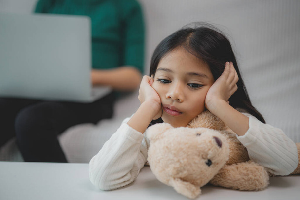 Ein junges Mädchen sitzt auf einer Couch, auf ihrem Schoß ein Teddybär. Sie ist traurig oder aufgebracht, vielleicht weil sie ihre Mutter vermisst - Foto, Bild