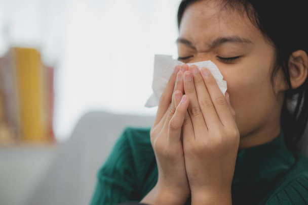 An unhealthy kid blowing their nose into a tissue, a Child suffering from running nose or sneezing, A girl catching a cold when the season change, a childhood wiping nose with a tissue - Photo, Image