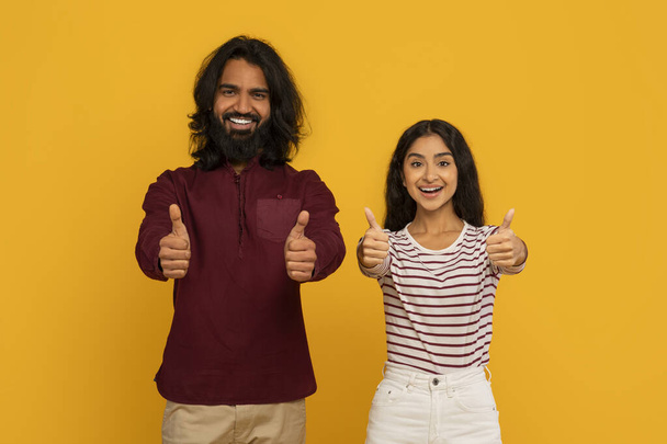 Both confidently giving a thumbs up, a man and woman stand side by side, exuding approval and positivity on yellow - Photo, Image