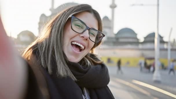 Een vrolijke vrouw met een bril glimlacht en poseert speels in de historische straten van Istanbul tijdens een heldere zonsondergang. - Video