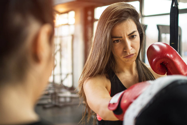 Beautiful brunette girl with red gloves exercising kick boxing at gym - Photo, Image