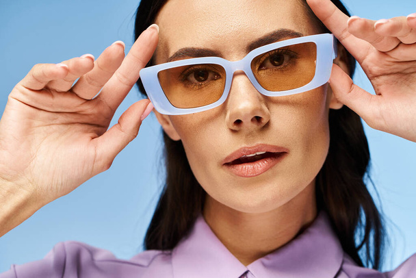 A fashionable woman in a purple shirt and blue sunglasses against a vibrant blue background. - Photo, Image