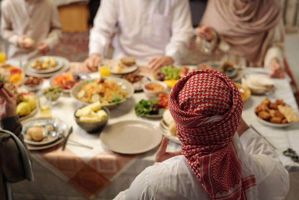 High angle view selective focus shot of unrecognizable Muslim man wearing keffiyeh having festive dinner with his family, copy space - Photo, Image