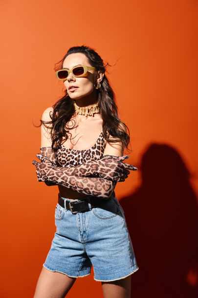 Tyylikäs nainen yllään leopardi tulostaa alkuun ja denim shortsit, tihkuu kesäisin vibes, oranssi tausta. - Valokuva, kuva