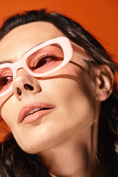 Una mujer de moda con gafas rosas y una camisa blanca emana vibraciones de verano sobre un fondo naranja. - Foto, Imagen