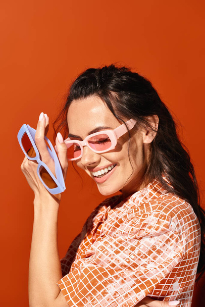 Mujer con estilo en gafas de sol sosteniendo tijeras juguetonamente cerca de su cara, mostrando creatividad y opciones de moda audaces. - Foto, Imagen