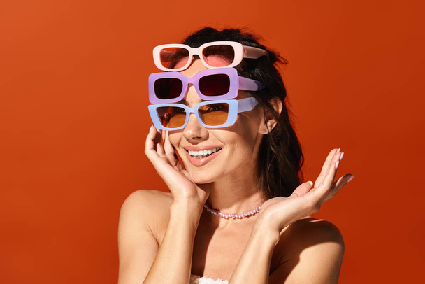 Стильна жінка з сонцезахисними окулярами вражає позу в студії на помаранчевому фоні. - Фото, зображення