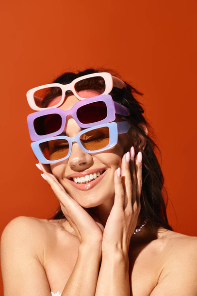 A stylish woman with sunglasses striking a pose in a studio, against an orange background, exuding summertime fashion vibes. - Photo, Image