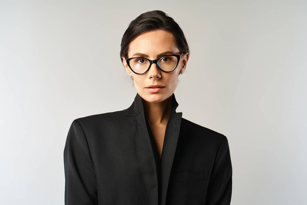 Una mujer elegante con gafas y una chaqueta negra posa sobre un fondo gris de estudio. - Foto, imagen