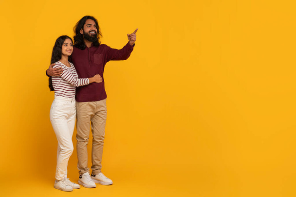 Com expressões animadas, um homem e uma mulher apontam para algo fora do quadro, invocando curiosidade em um fundo amarelo. - Foto, Imagem