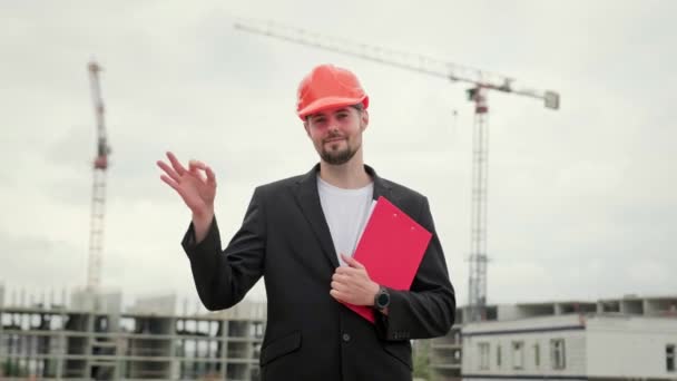 Construtor profissional em terno de escritório e protetor capacete laranja segurando prancheta e mostrando sinal ok. Movimento lento - Filmagem, Vídeo